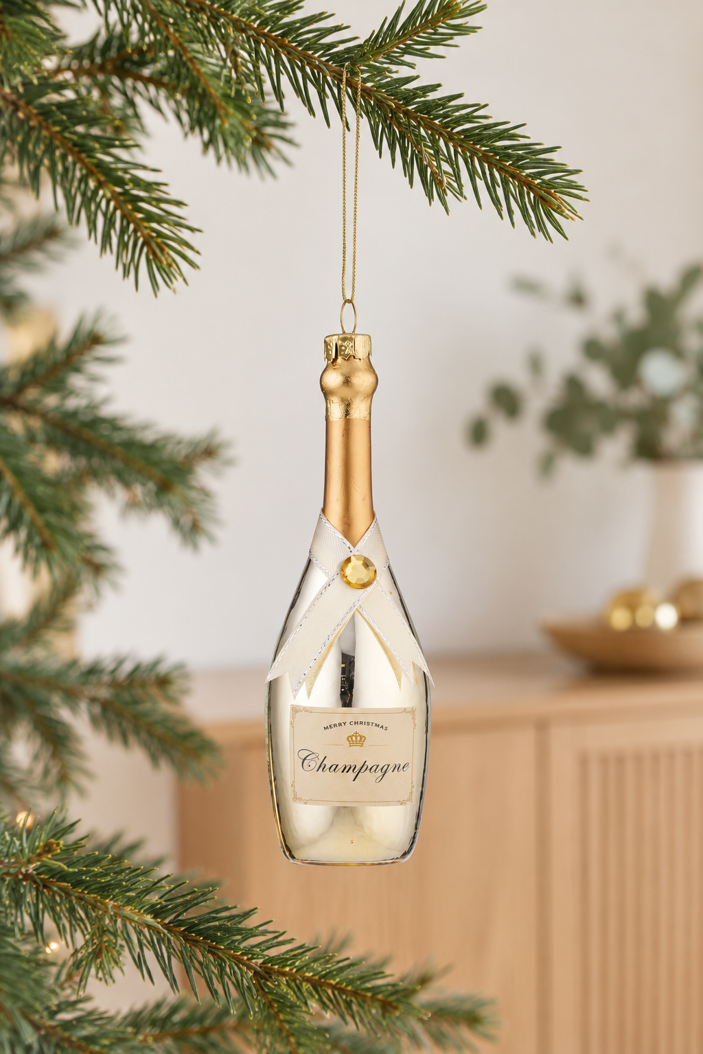 Gold champagne bottle glass ornament hanging indoors in bright summer daylight