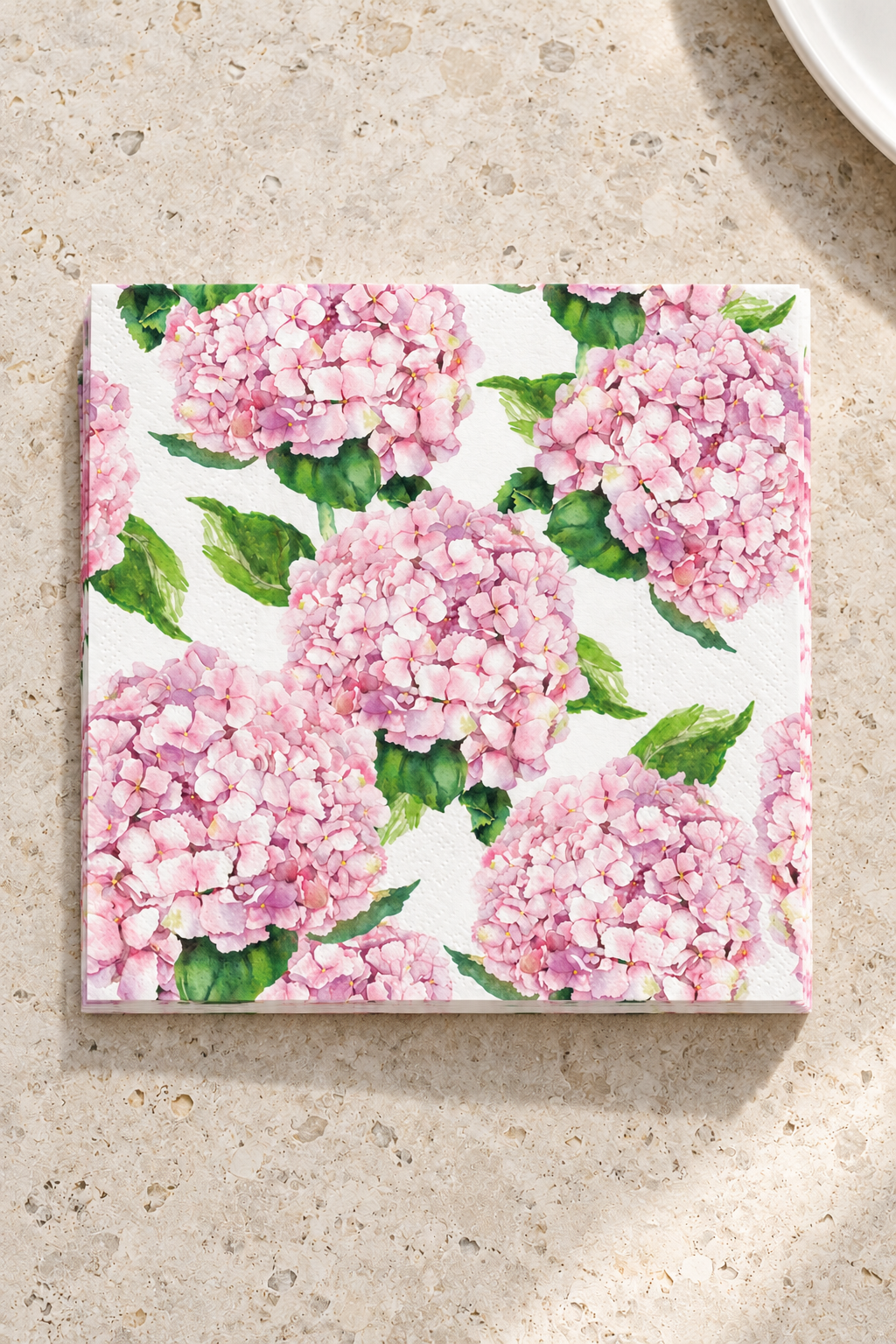 Hydrangea Paper Napkins - Pink in a precisely aligned thin paper stack, viewed overhead on a pale stone bench; Coast to Coast KW5357
