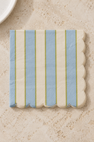 Carnival Paper Napkins - Blue and Ivory in a neat thin paper stack, viewed overhead on a natural stone bench; Coast to Coast KW5519