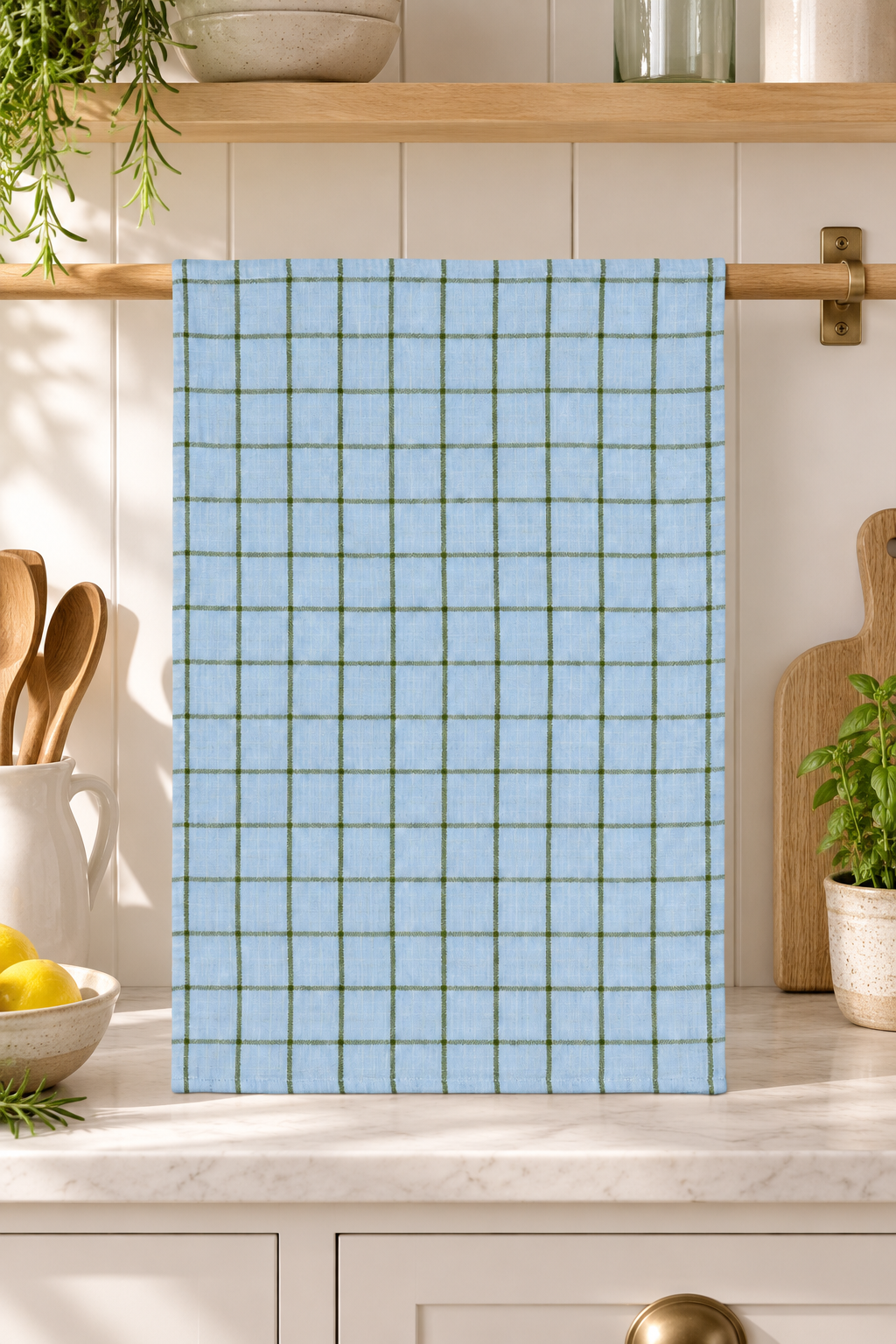 Pale blue Kit tea towel with olive green checks draped in a sunlit coastal kitchen