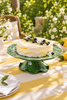 Green cabbage melamine cake stand styled with a lemon and blueberry cake on a yellow and white striped garden table