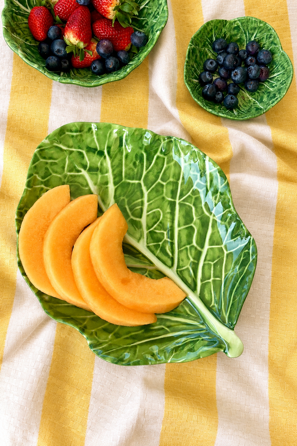 Green Stemmed Platter – Cabbage Melamine styled with melon and berries on yellow and white striped tablecloth